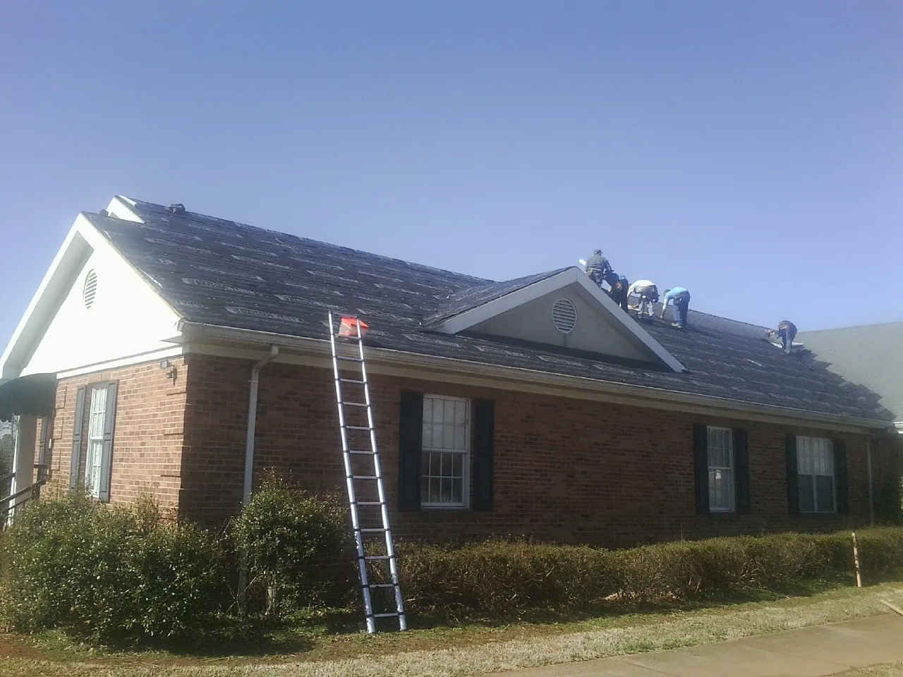 Crew tearing shingles off a brick ranch roof with a ladder set — Emergency Roof Repair work by our crew in Valley View