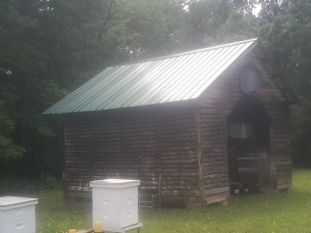 Green metal roof on a weathered barn beside stacked beehives in Valley View
