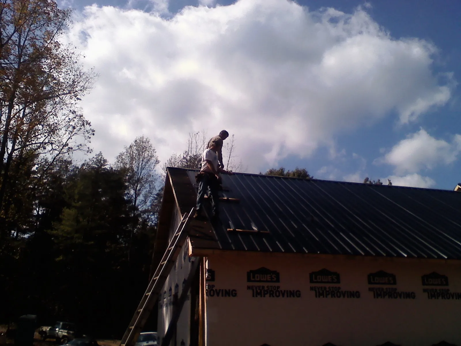 Roofer fastening dark metal panels high against a cloudy sky, from a Roof Inspection job in Valley View